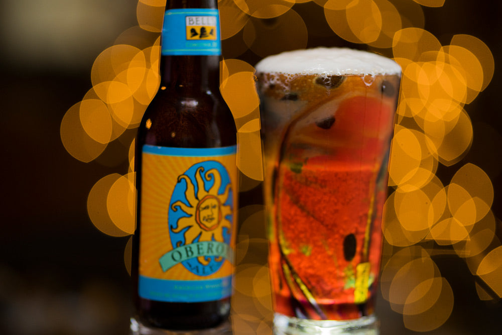 Derek DeYoung Cutthroat Trout Flank pilsner glass with a beer bottle and warm background lights